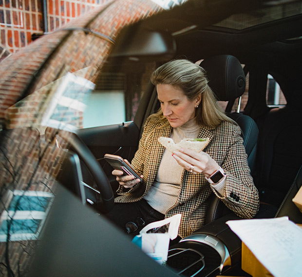 Business woman eating lunch in her car and using her phone